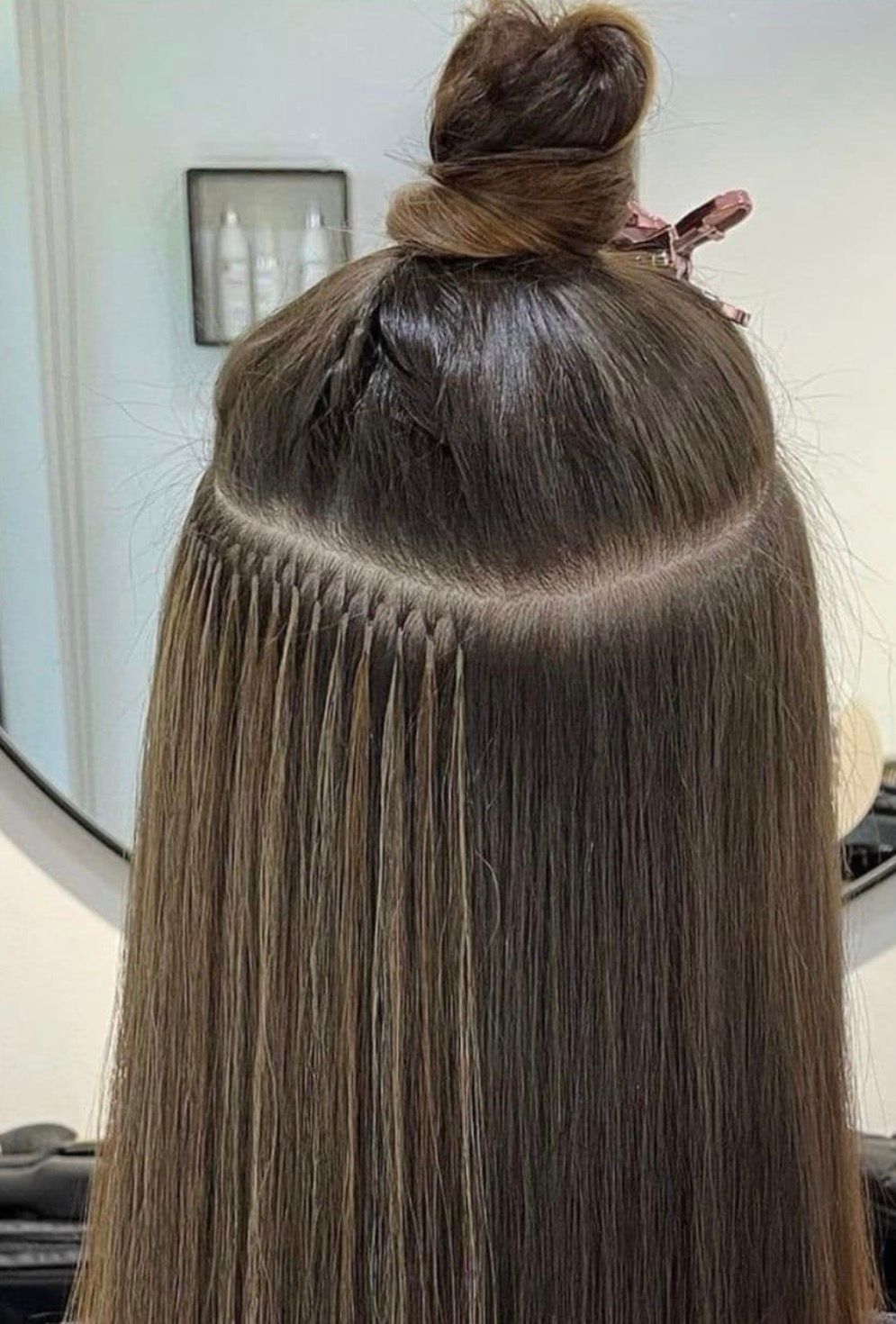 Close-up rear view of brown hair with microbead hair extensions visible in a horizontal row at the crown.