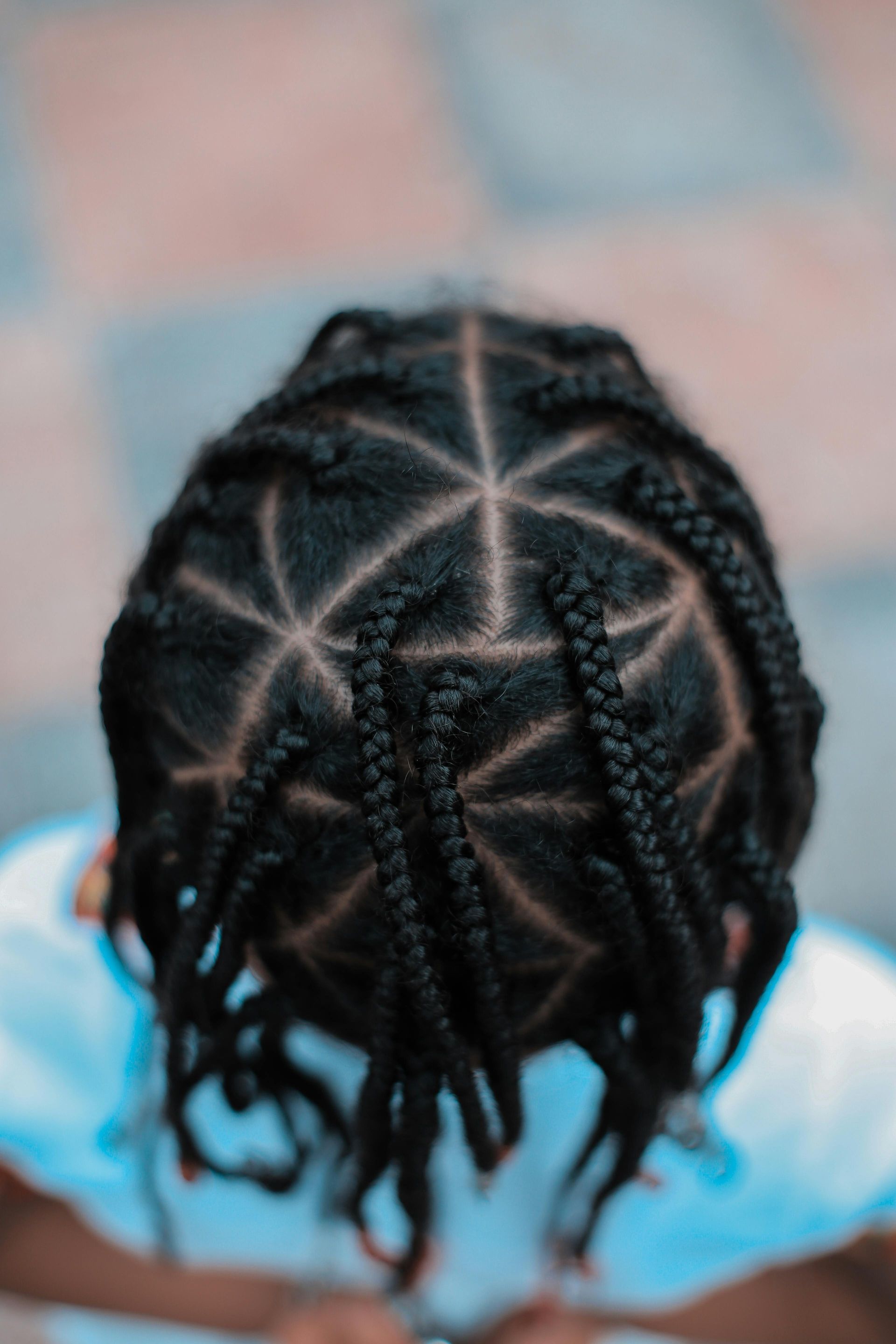 A top-down view of hair styled in neat, triangular parted sections that lead into individual black braids.