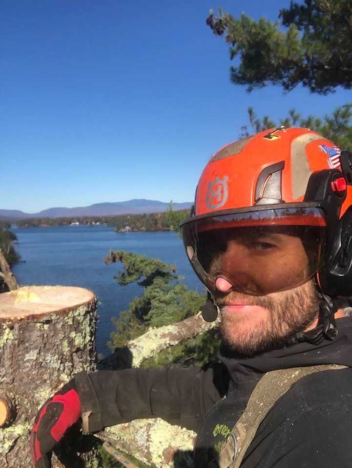 A man wearing a helmet is standing next to a tree stump.
