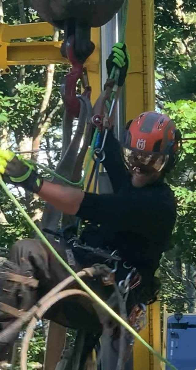 A man wearing a helmet and gloves is climbing a crane.