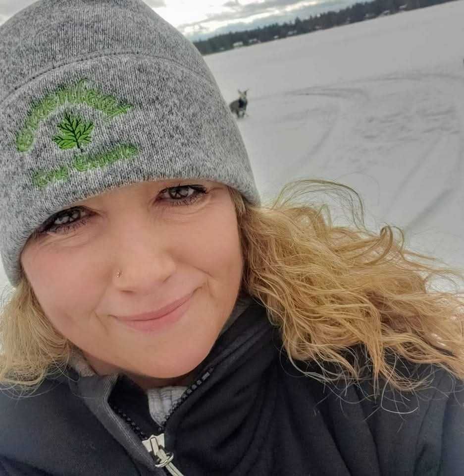 A woman wearing a gray beanie and a black jacket is smiling in the snow.