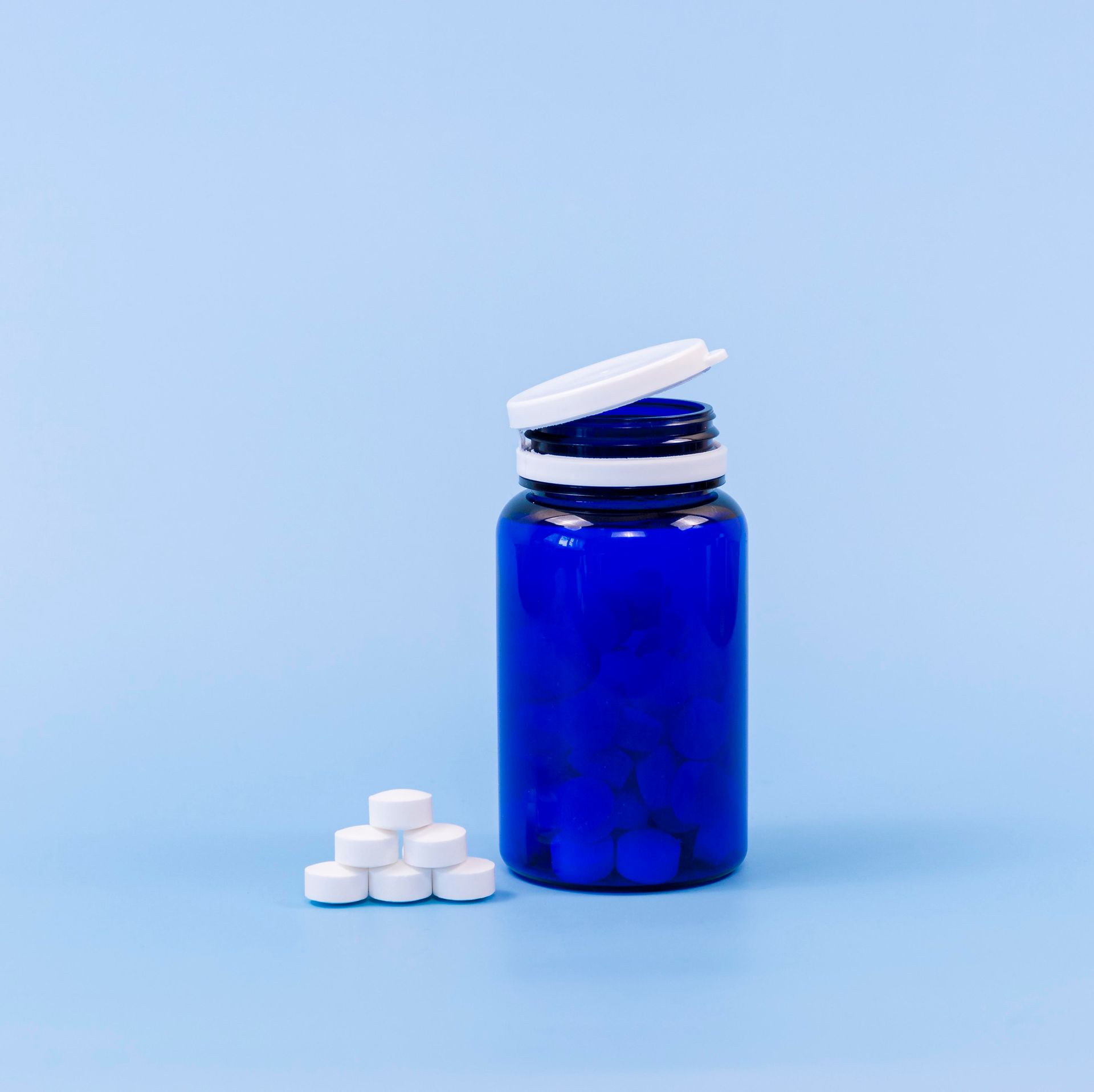 a blue bottle filled with white pills on a blue background .