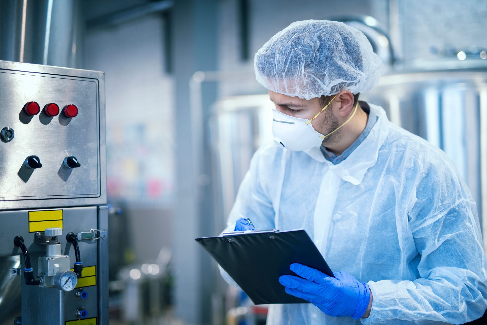 a man wearing a mask and gloves is holding a clipboard in a factory .