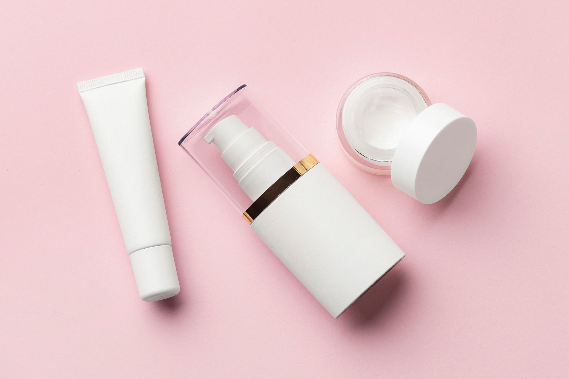 three white bottles of cosmetics on a pink background .