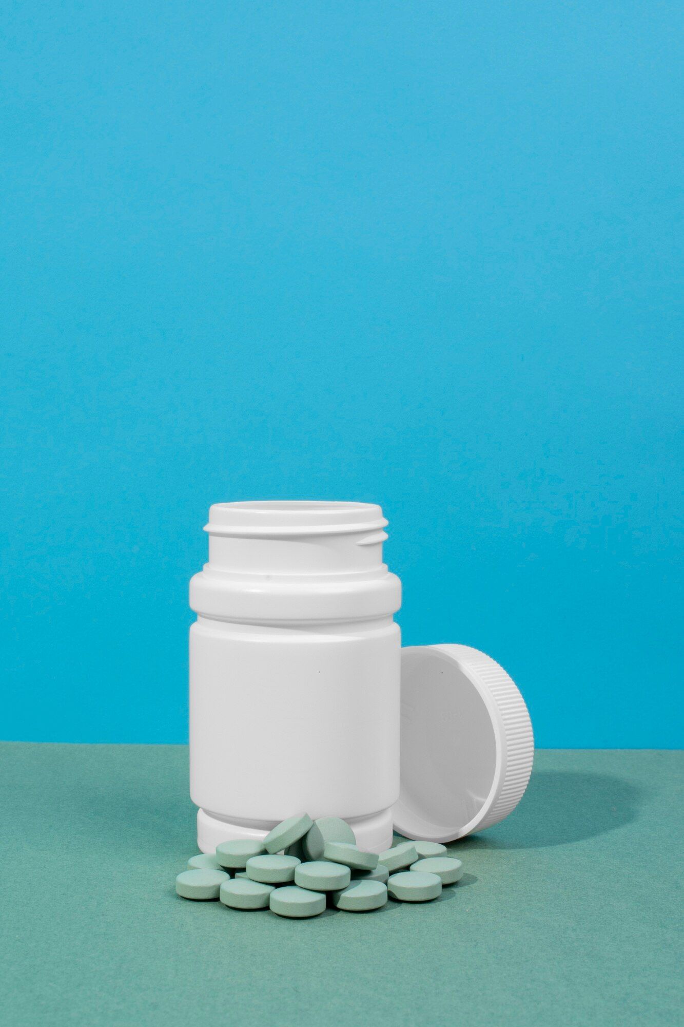 a white bottle filled with green pills on a blue background .