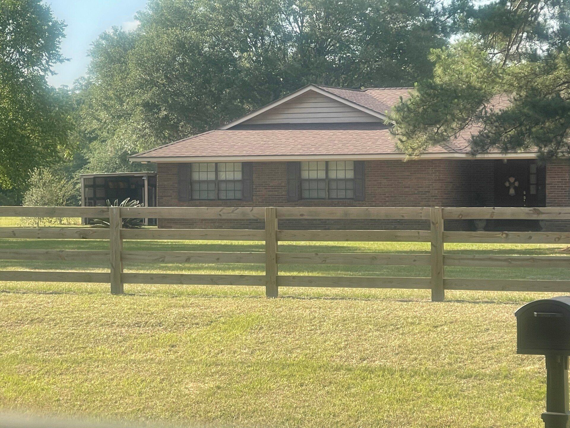 Brown brick house with a wooden fence and a mailbox in a grassy yard.