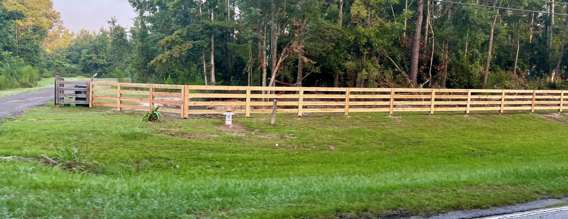 A wooden fence bordering a grassy area with trees in the background. A mailbox is visible.