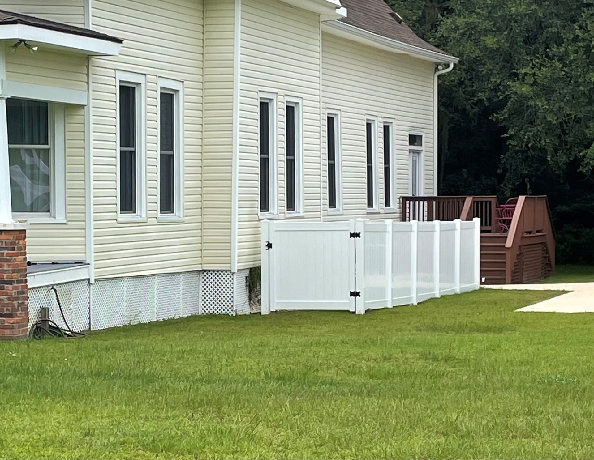 White house with white fence and wooden deck on green grass.