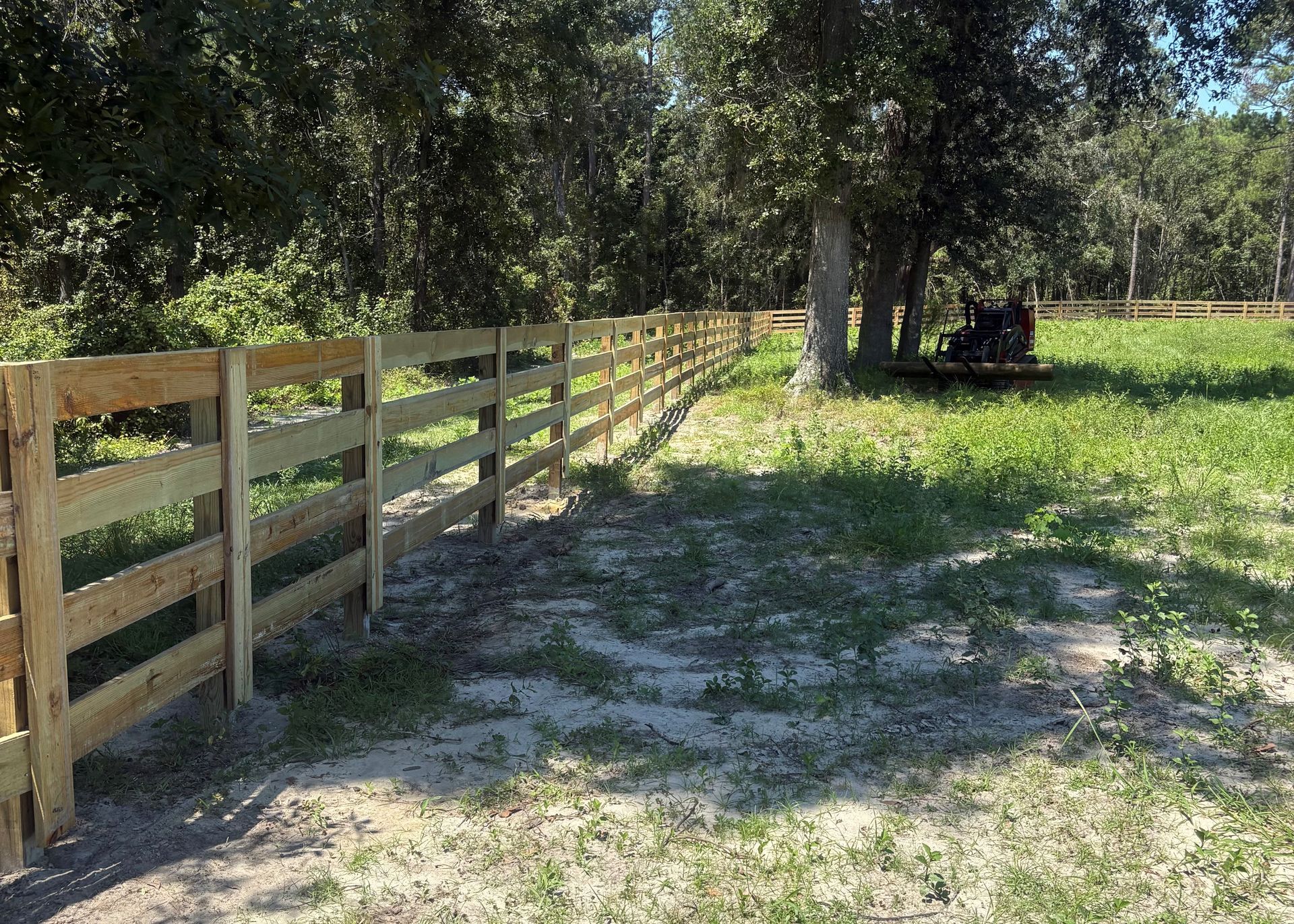 Wooden fence in a field with trees in the background on a sunny day.