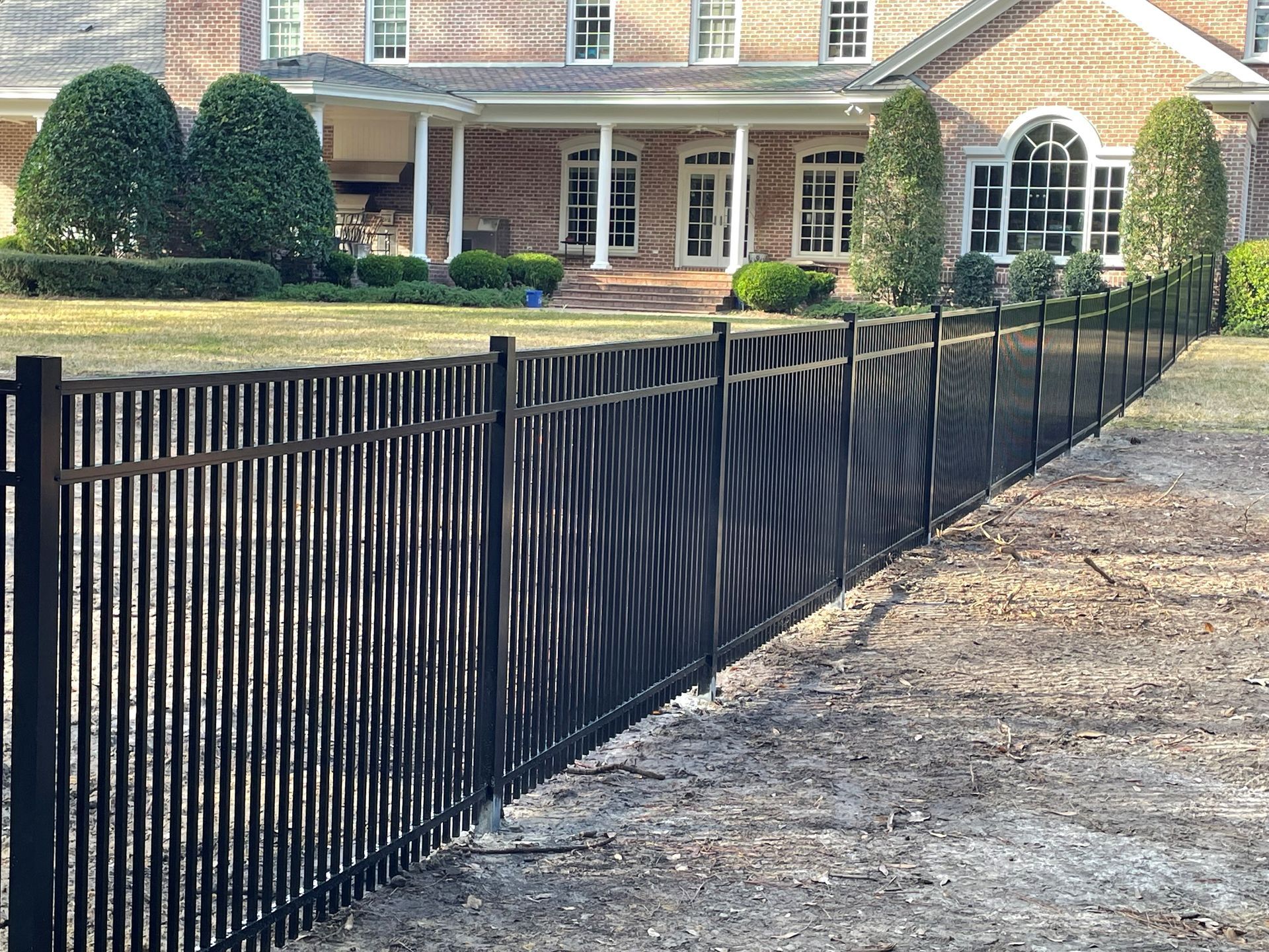 Black metal fence in front of a brick house with a lawn.