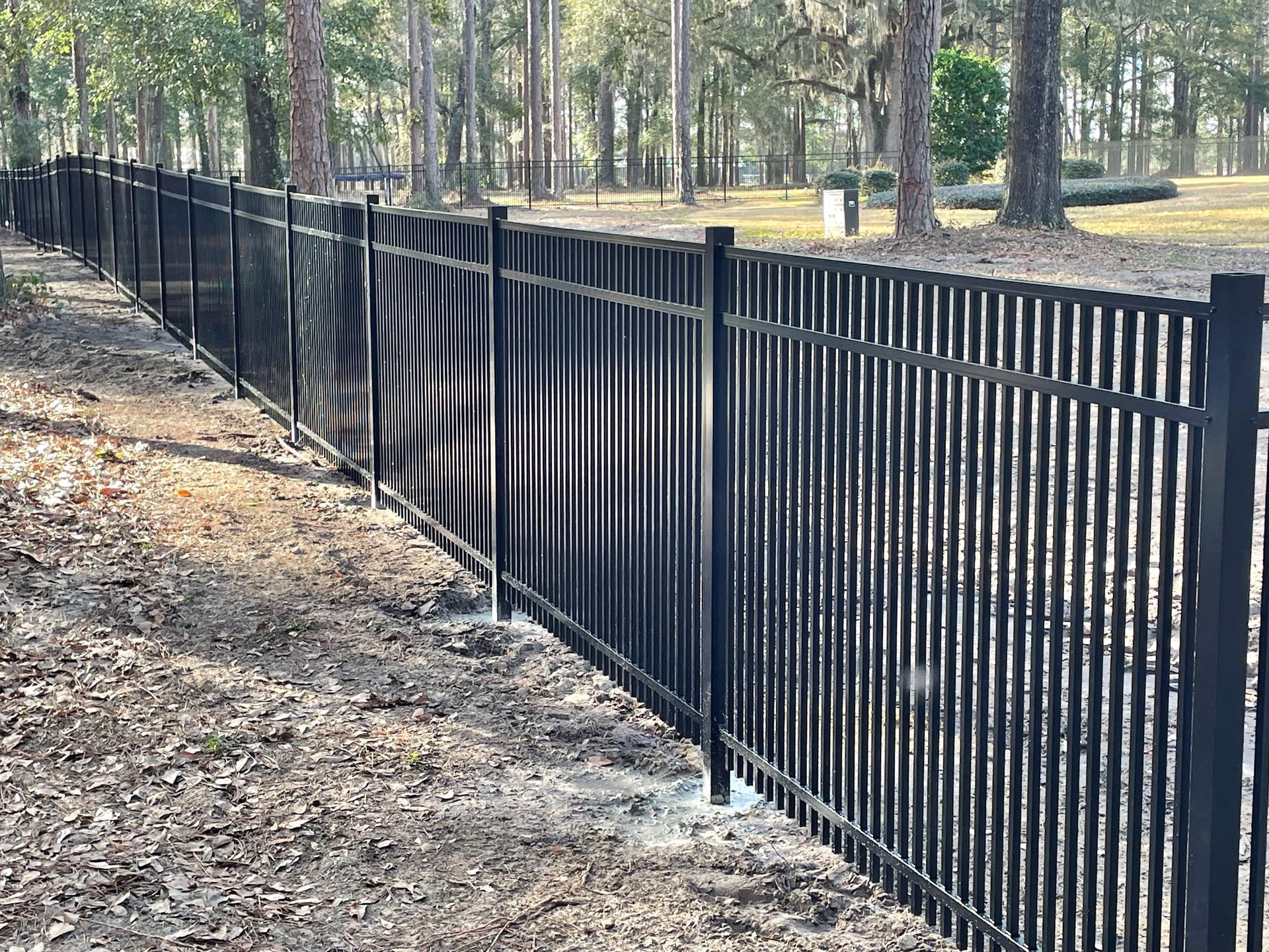 Black metal fence in a grassy area, trees in the background.