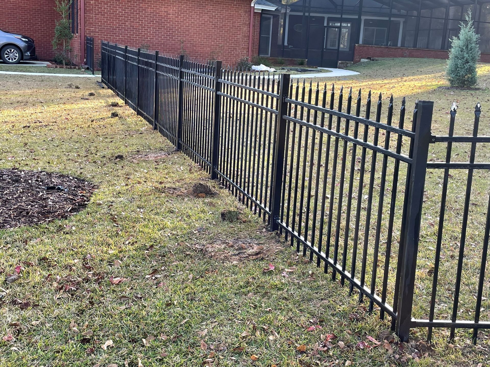 Black metal fence along a grassy yard, with a home and foliage in the background.