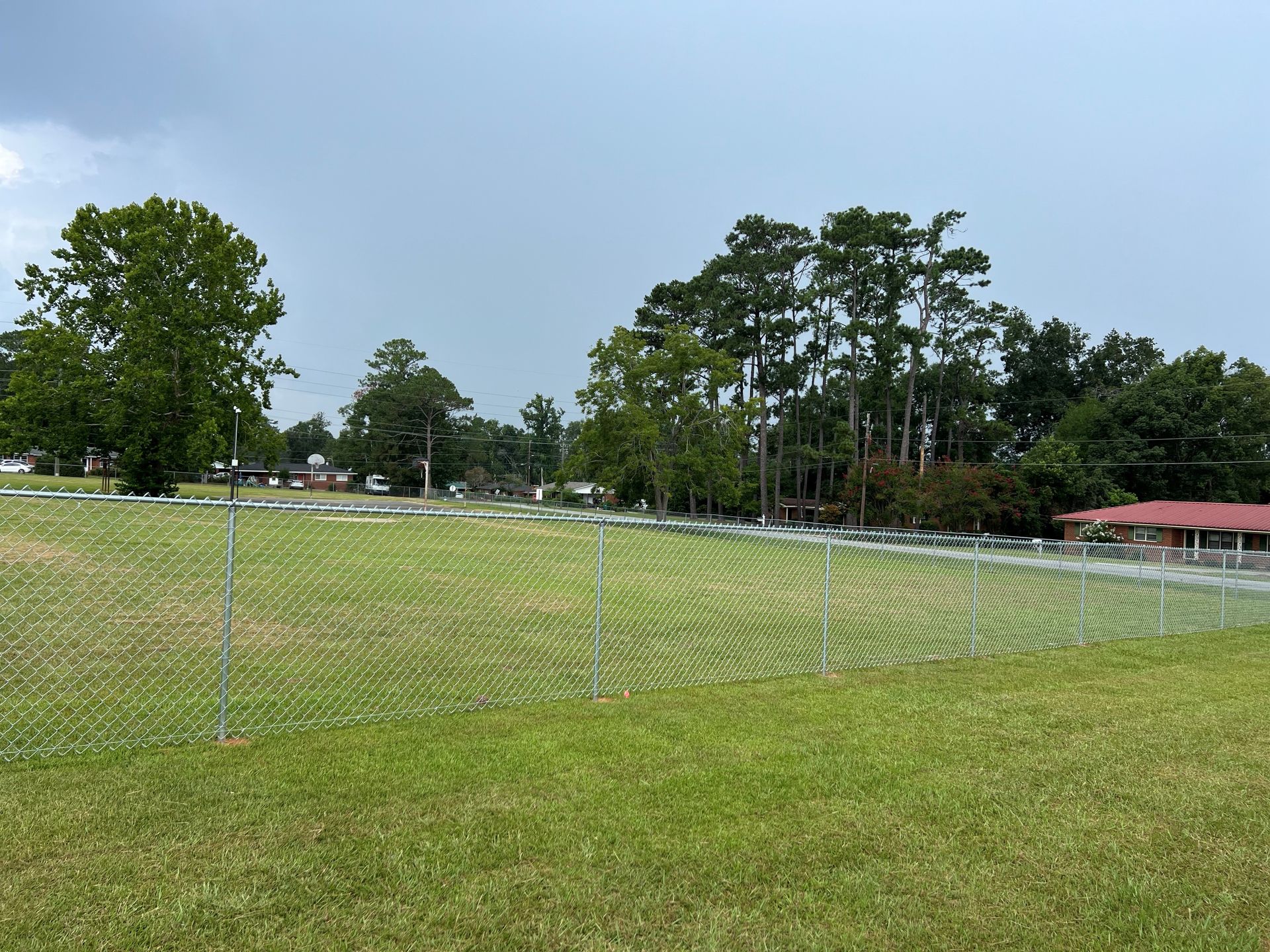 Grassy field with chain-link fence, trees, and overcast sky in the background.