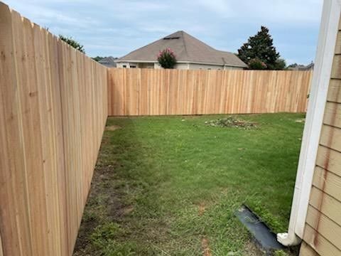 Wooden fence surrounds a small backyard with green grass. A house is visible in the background.