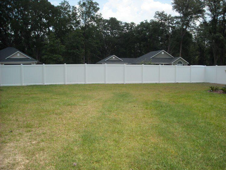 White vinyl fence surrounding a grassy backyard with houses and trees in the background under a cloudy sky.