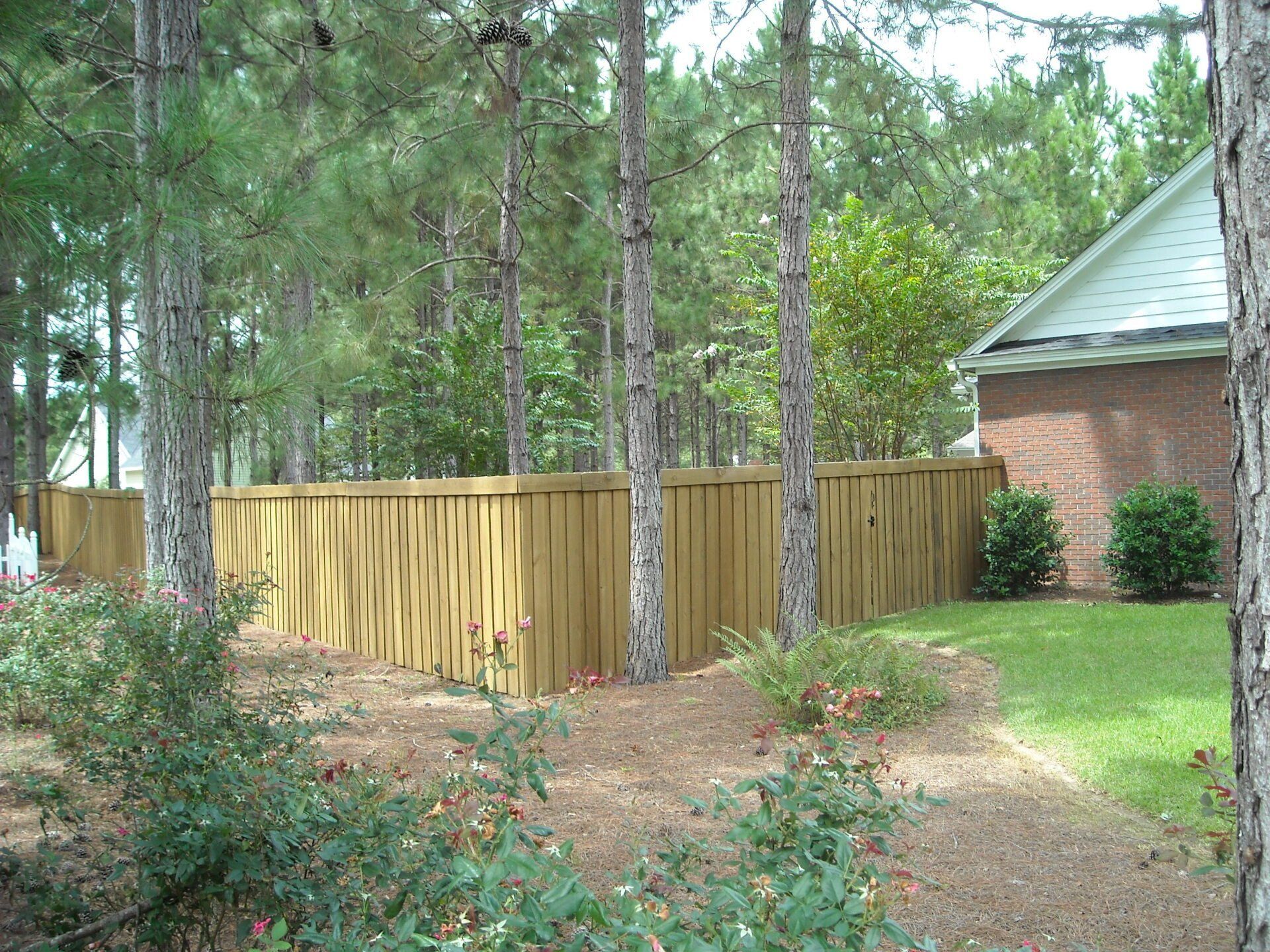 Wooden fence bordering a grassy yard with trees, next to a brick house.
