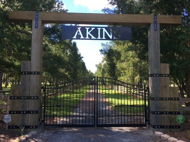 Entrance gate to Akin ranch with wooden posts, metal sign, and wrought iron gates.