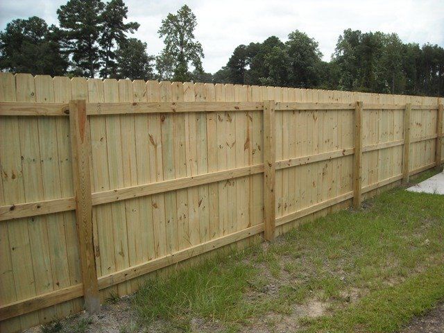 Wooden fence in a grassy yard, with tall green trees in the background.