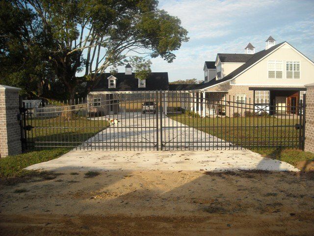 Black metal gate leading to a driveway with buildings and landscaping in the background.