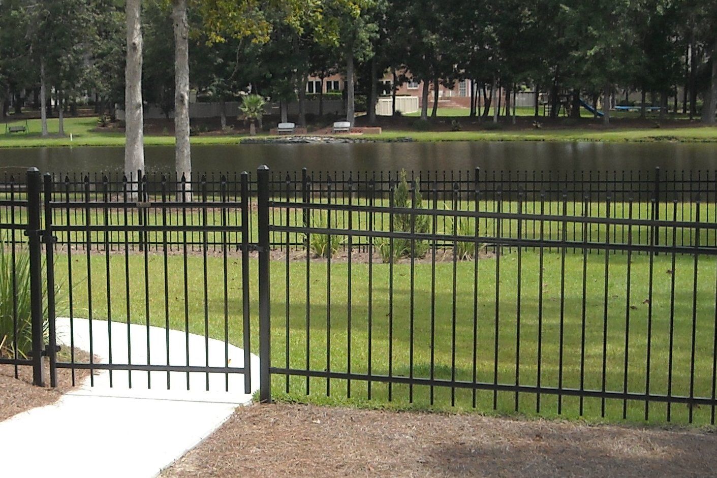Black metal fence surrounding green grass and a body of water.