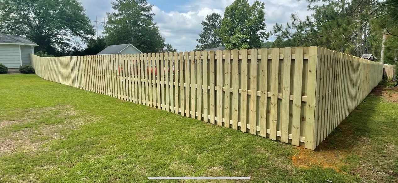 A wooden fence in a grassy yard curves around a corner.