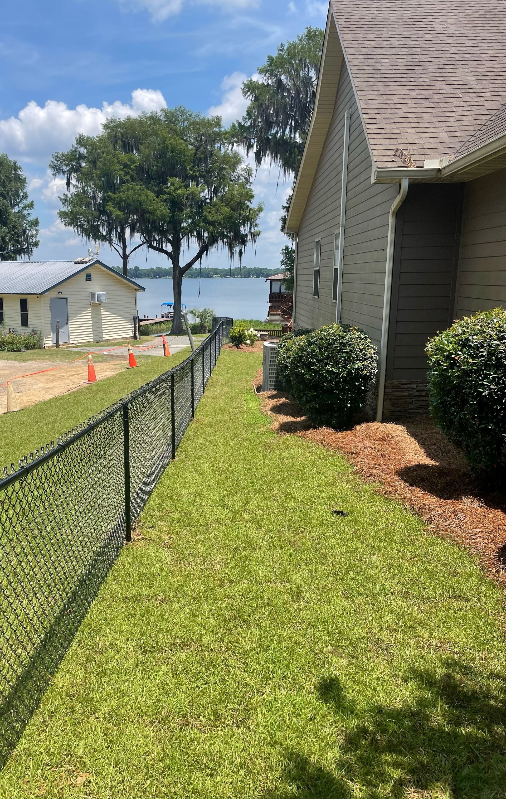 Lawn alongside a house with a black chain-link fence separating it from a dirt path leading to a waterfront.