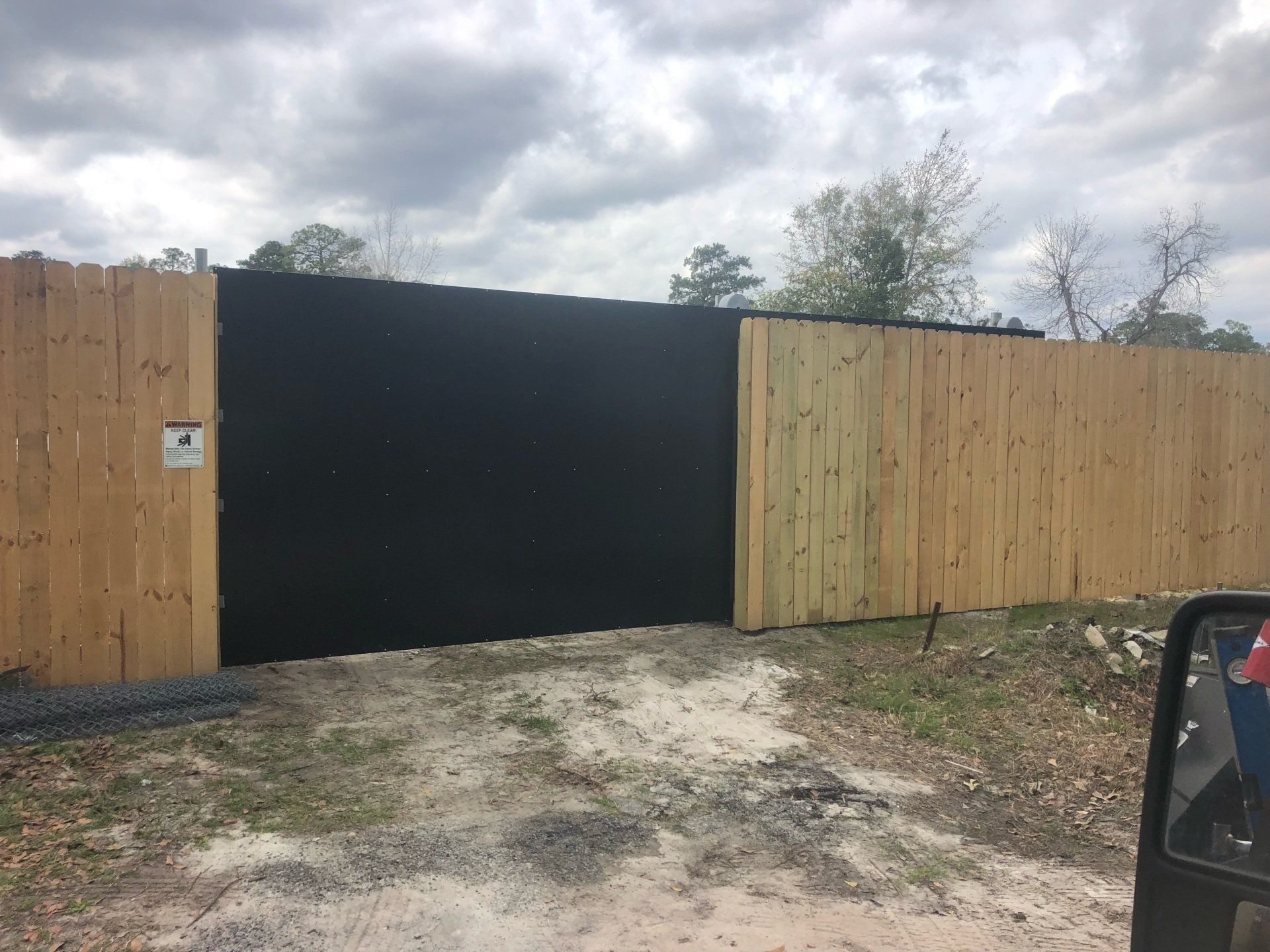 Wooden fence with a large black gate; gravel ground.