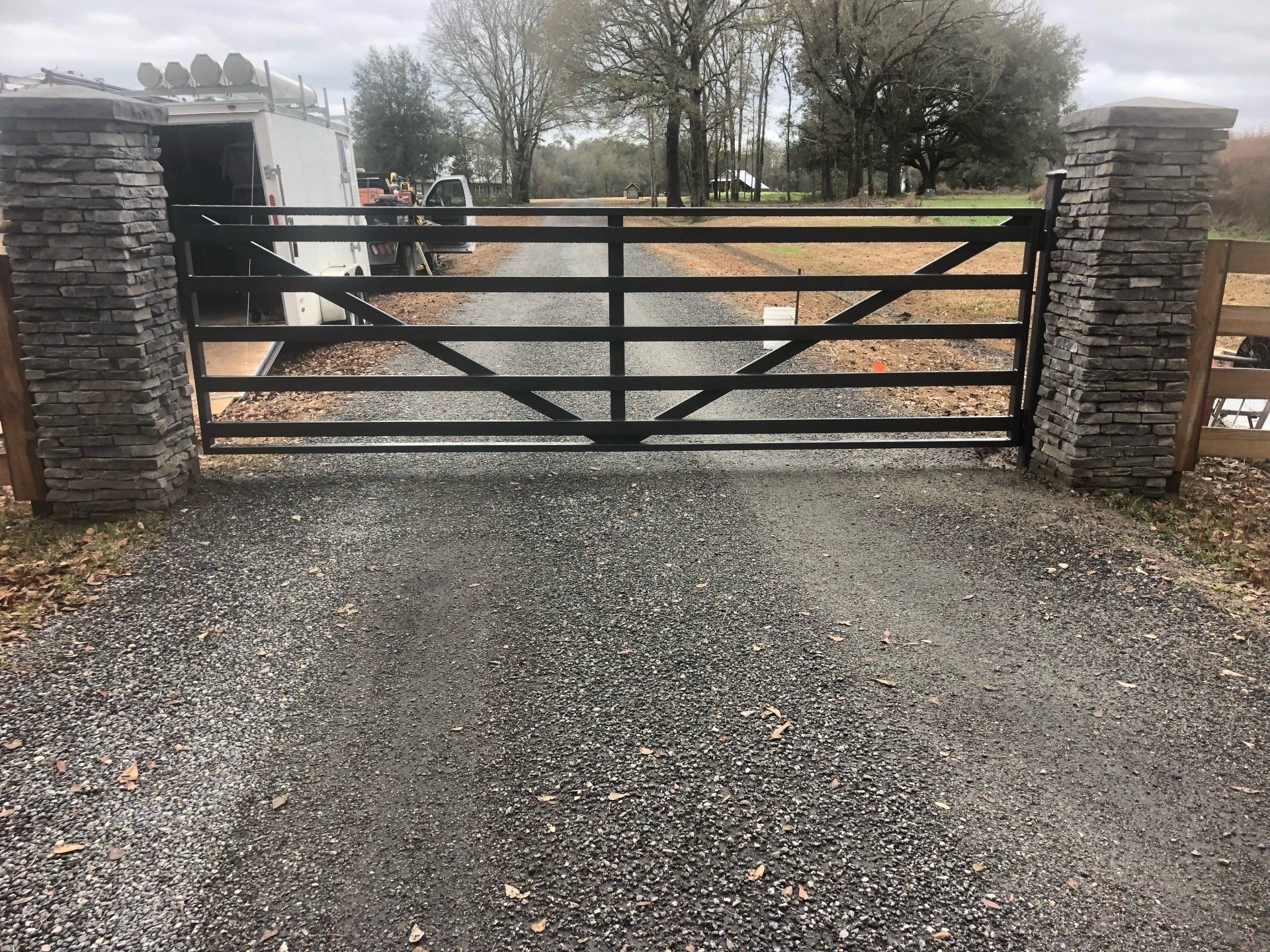Black metal gate with stone pillars at gravel driveway entrance.