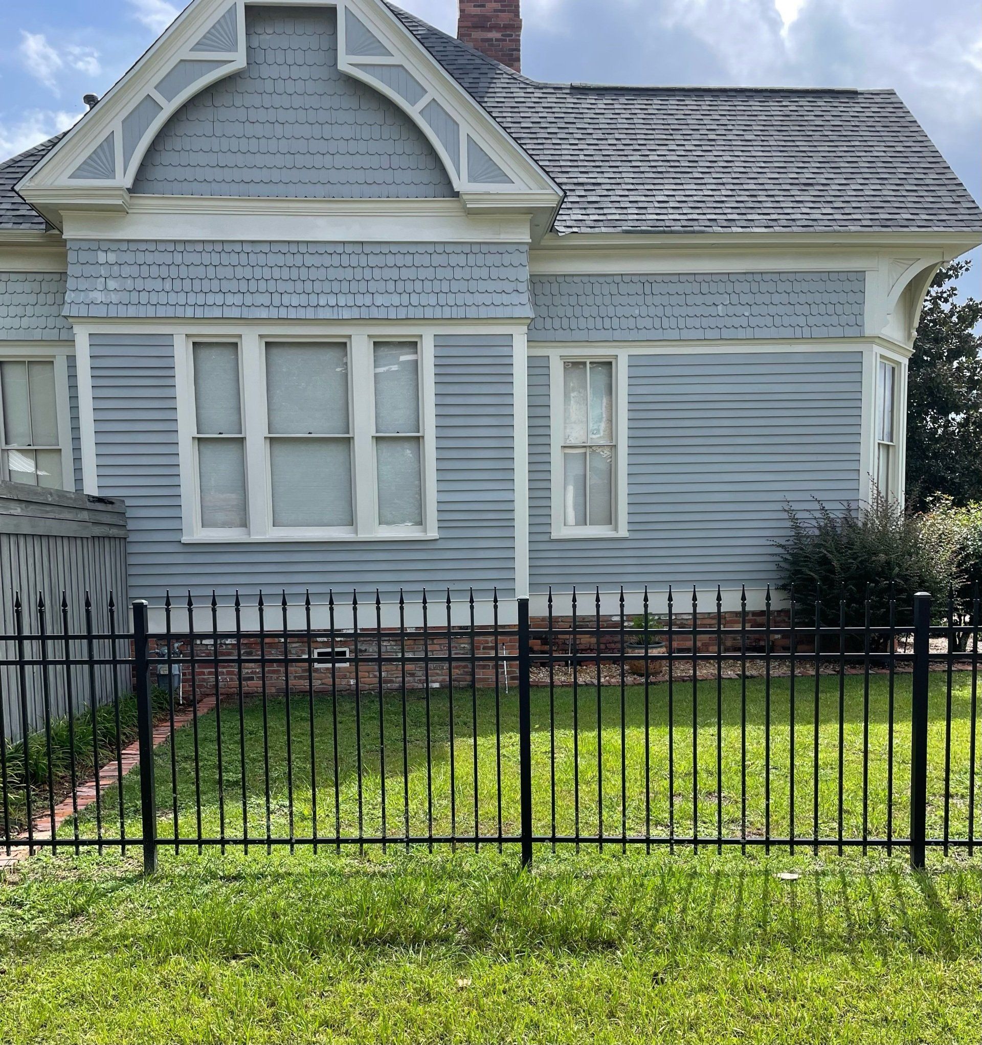 Blue Victorian house with a black metal fence in front.