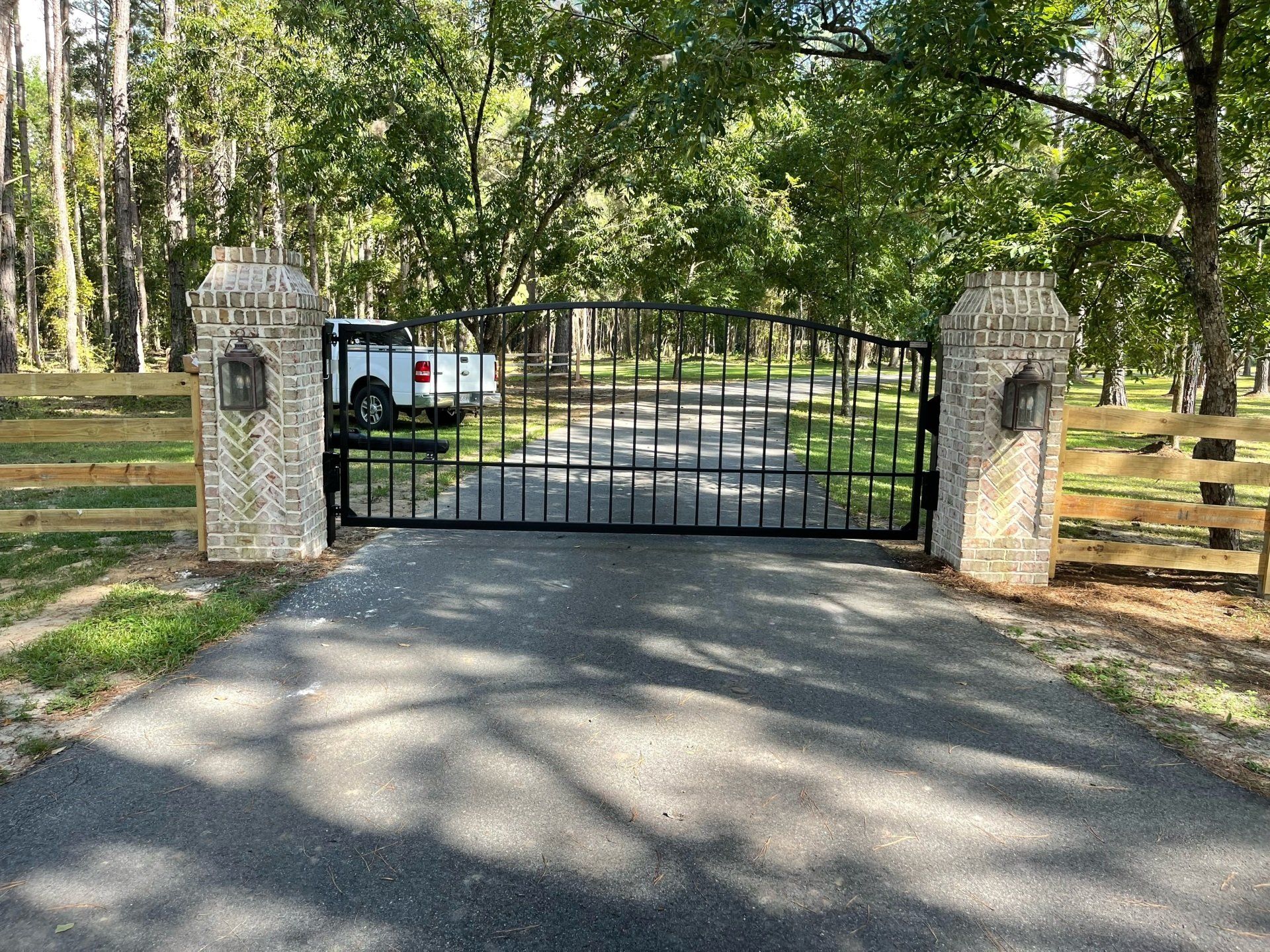 Black iron gate and stone columns at the entrance to a long driveway. A truck is parked beyond the gate.