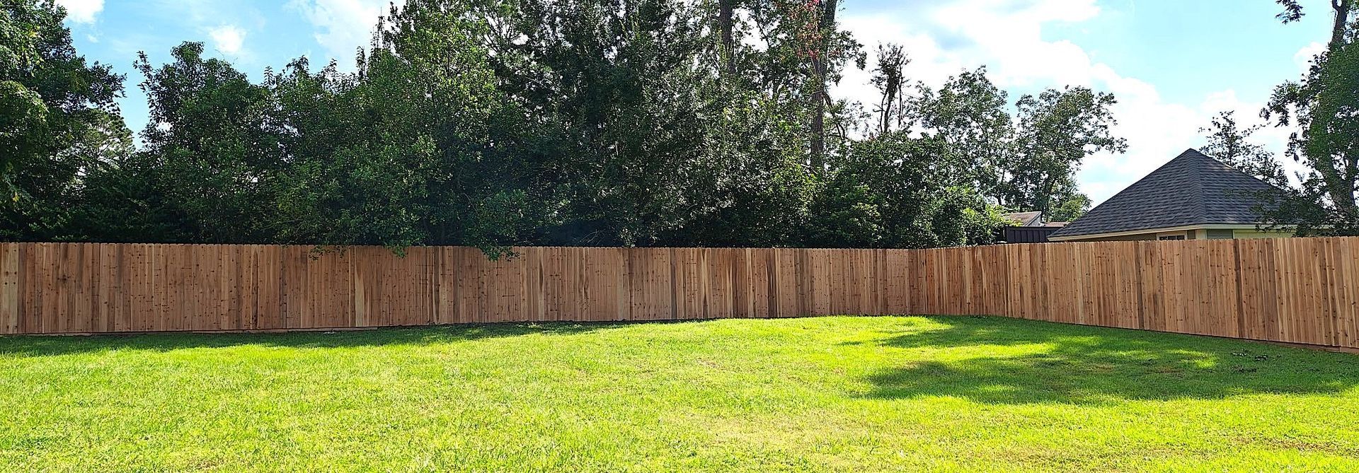 A wooden fence surrounds a green lawn, with trees behind it and a blue sky above.