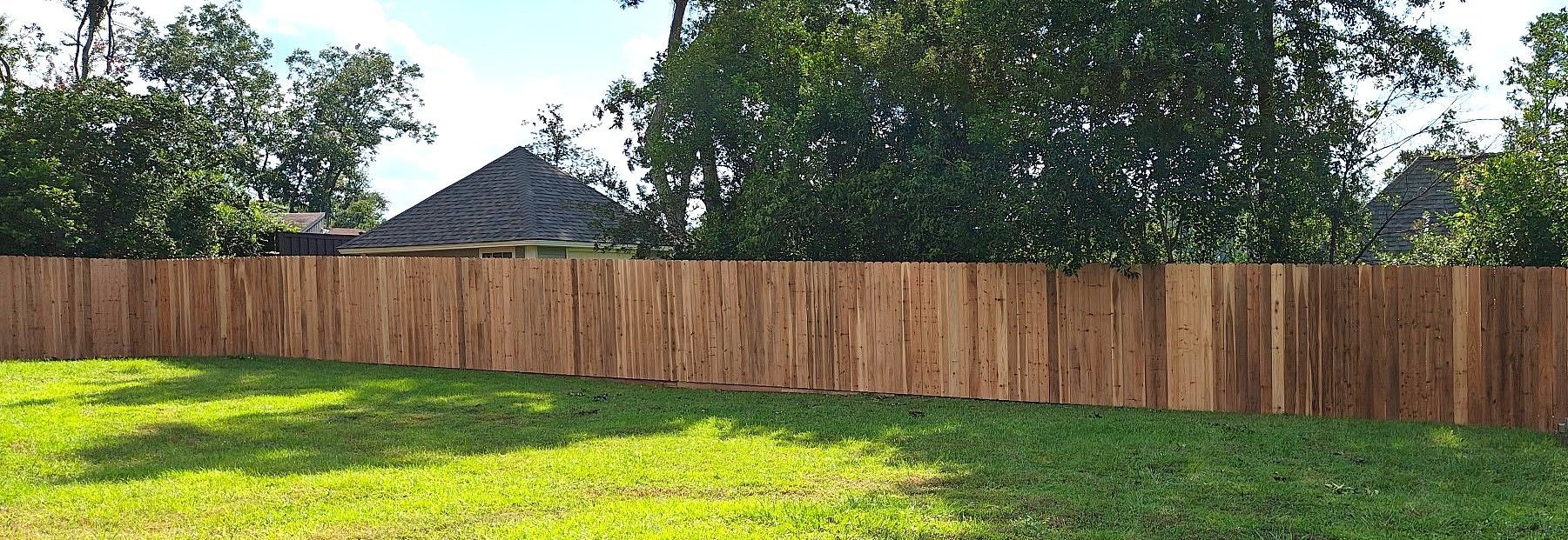 Wooden fence in front of a green grassy lawn. Trees and a house are in the background.