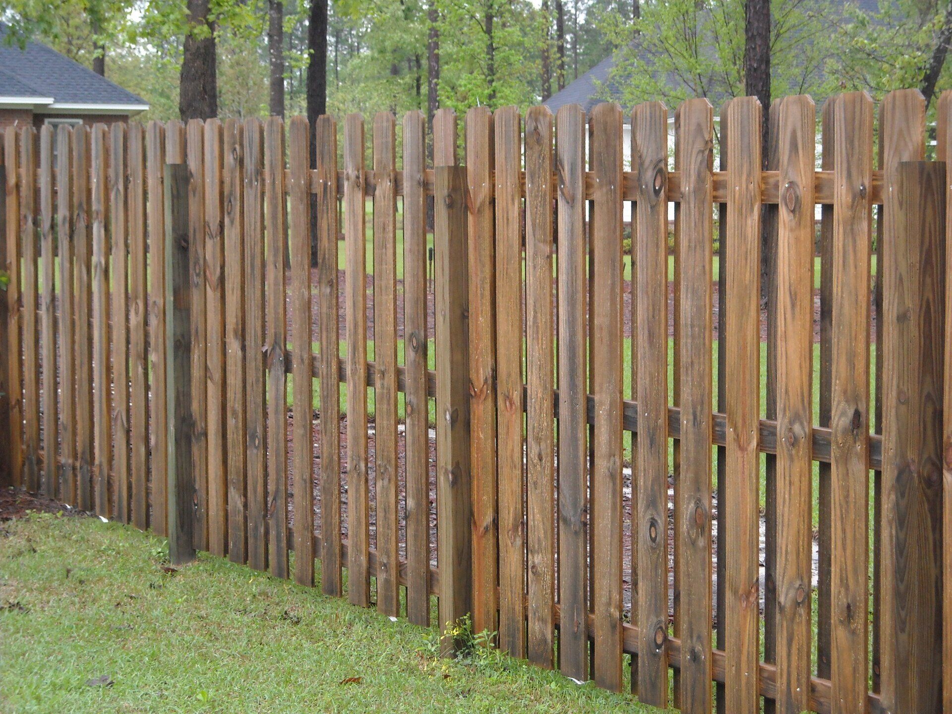 Wooden picket fence in a grassy yard, surrounded by trees.