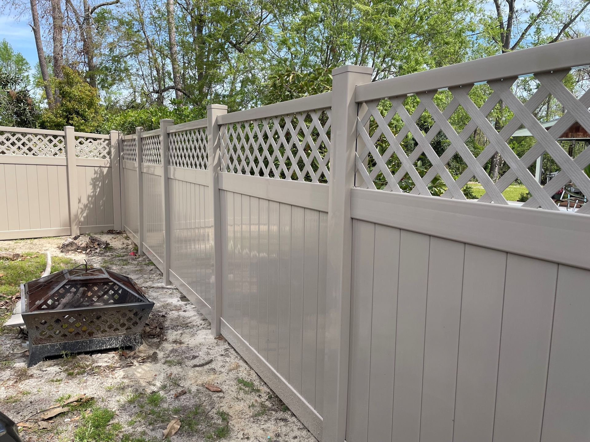 Tan vinyl fence with lattice top, in a backyard setting.