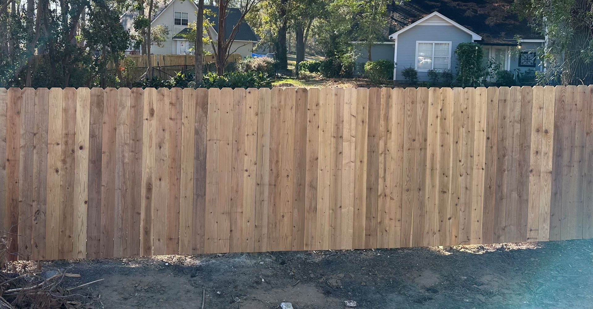 Wooden fence in front of two houses, trees in the background, daytime.