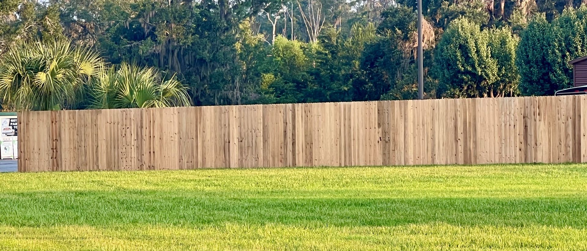 A wooden fence in front of green grass with trees and foliage in the background.