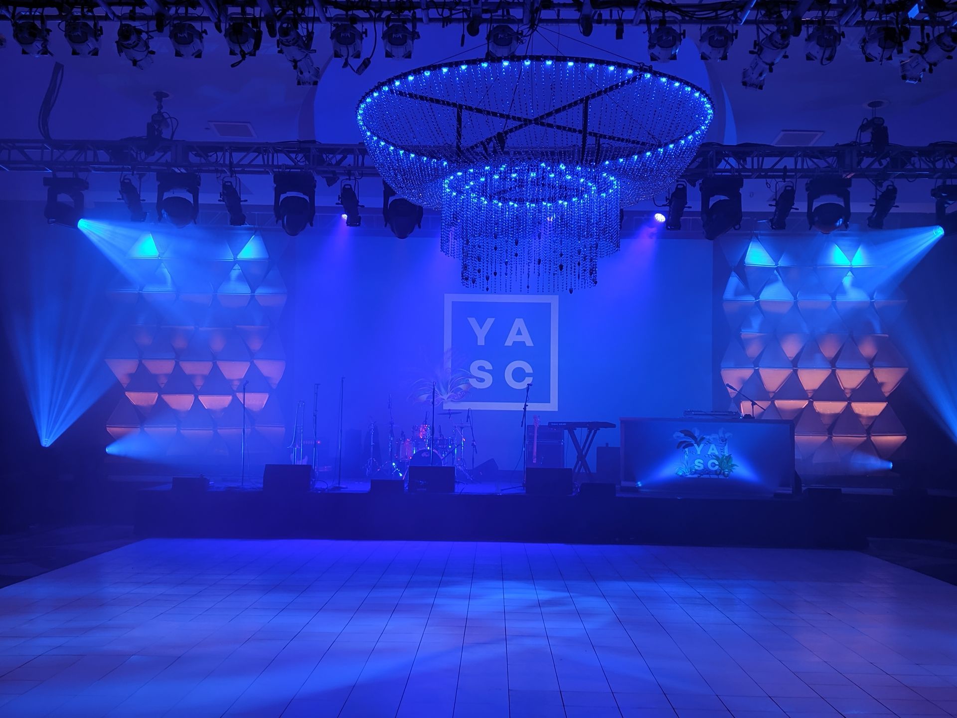 Stage lit with blue lights, a chandelier, and logo. Empty dance floor.