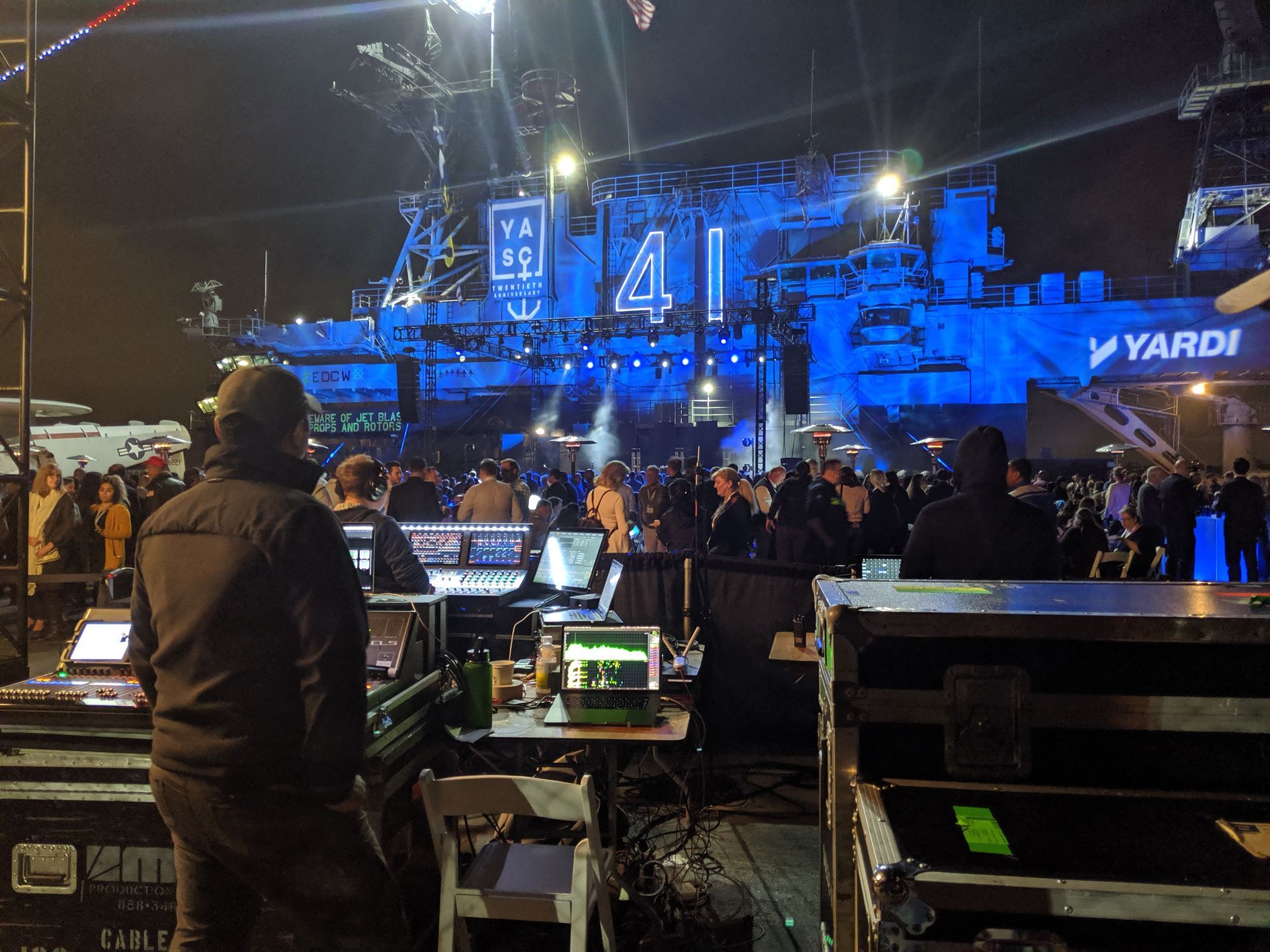 Concert stage at night with a crowd; audio engineers in front of a giant blue structure, Yardi 