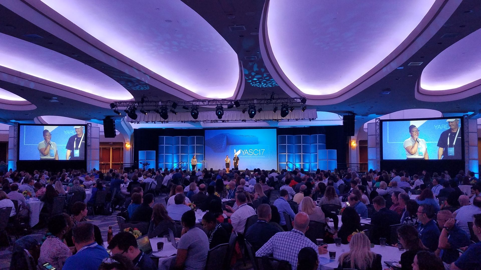 Large conference hall with a crowd attending a presentation on a stage.