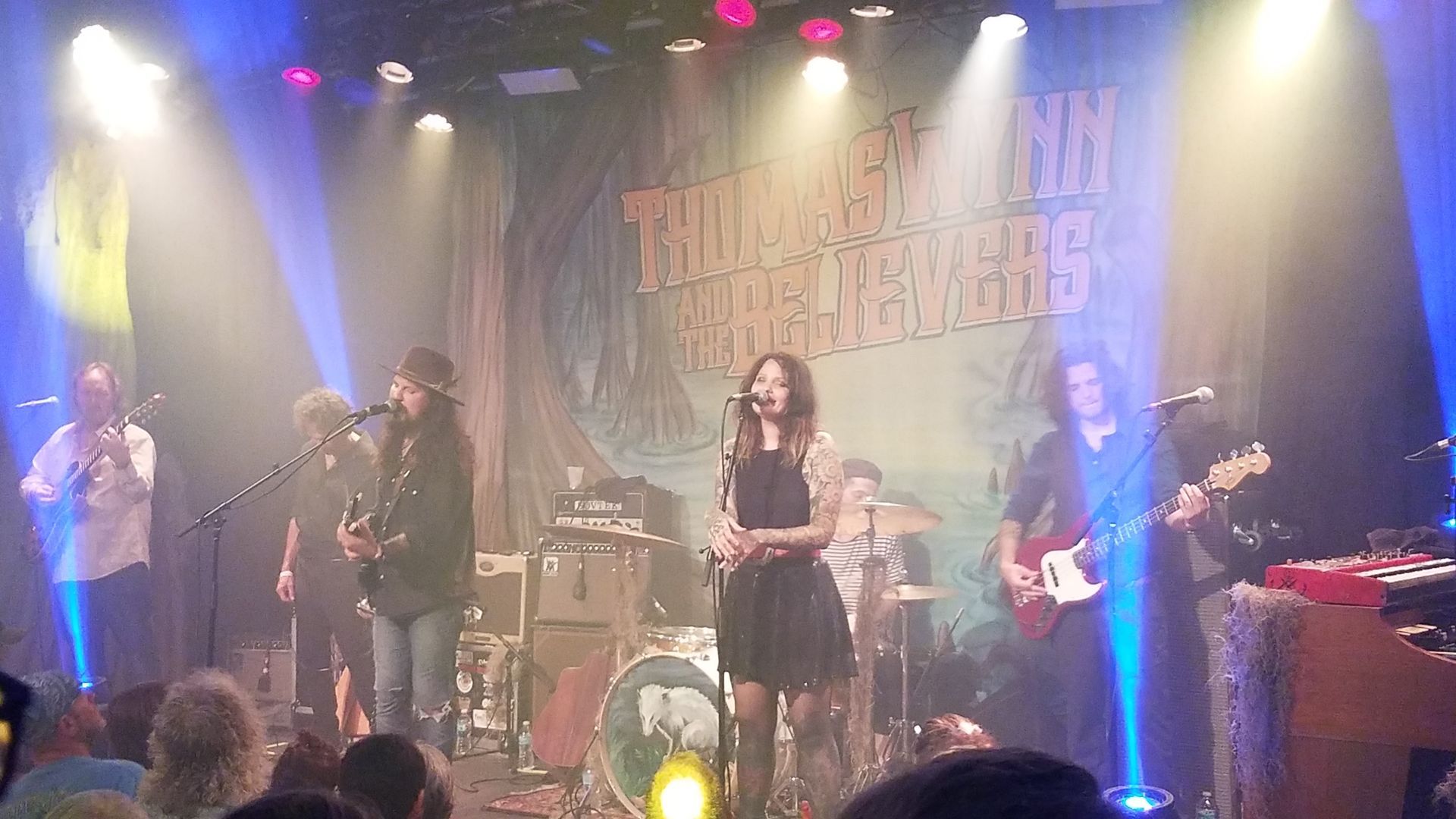 A band, The Lone Bellow, performs on stage with lights and a crowd. The lead singer is in the center.