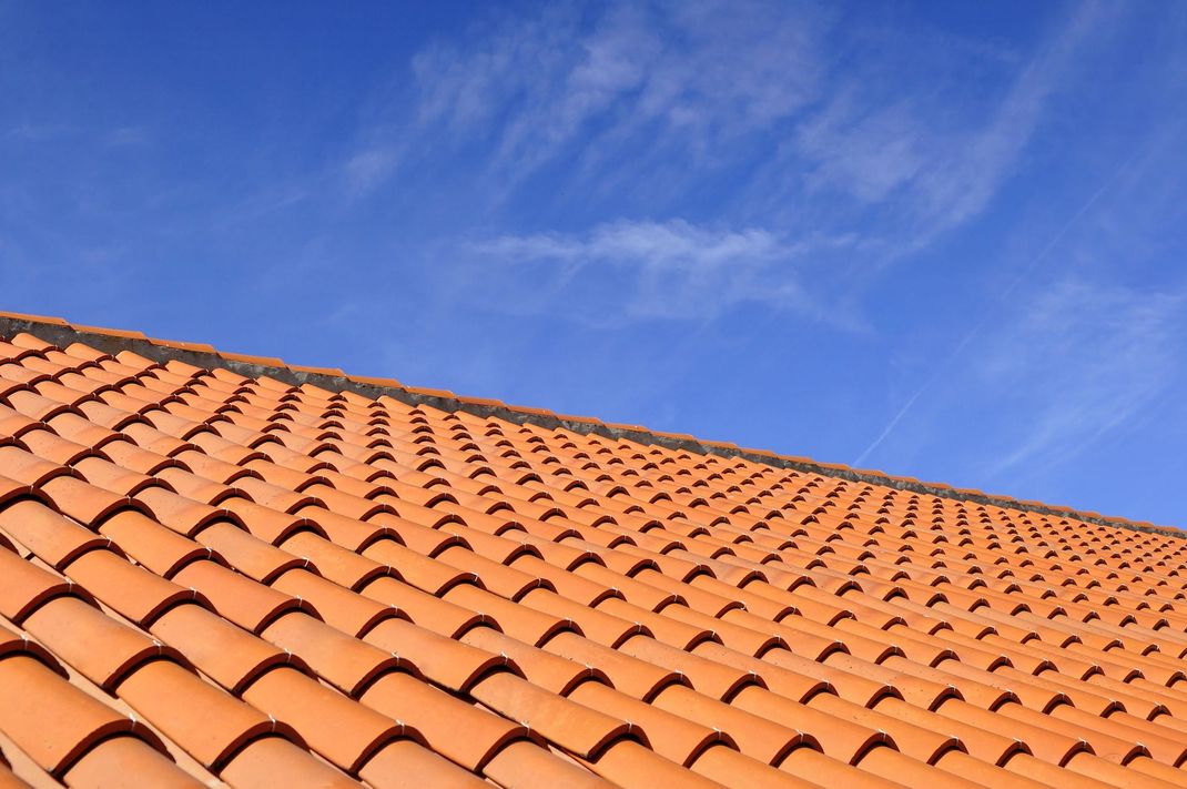 Un primo piano di un tetto di tegole di terracotta arancioni sullo sfondo di un cielo azzurro limpido.