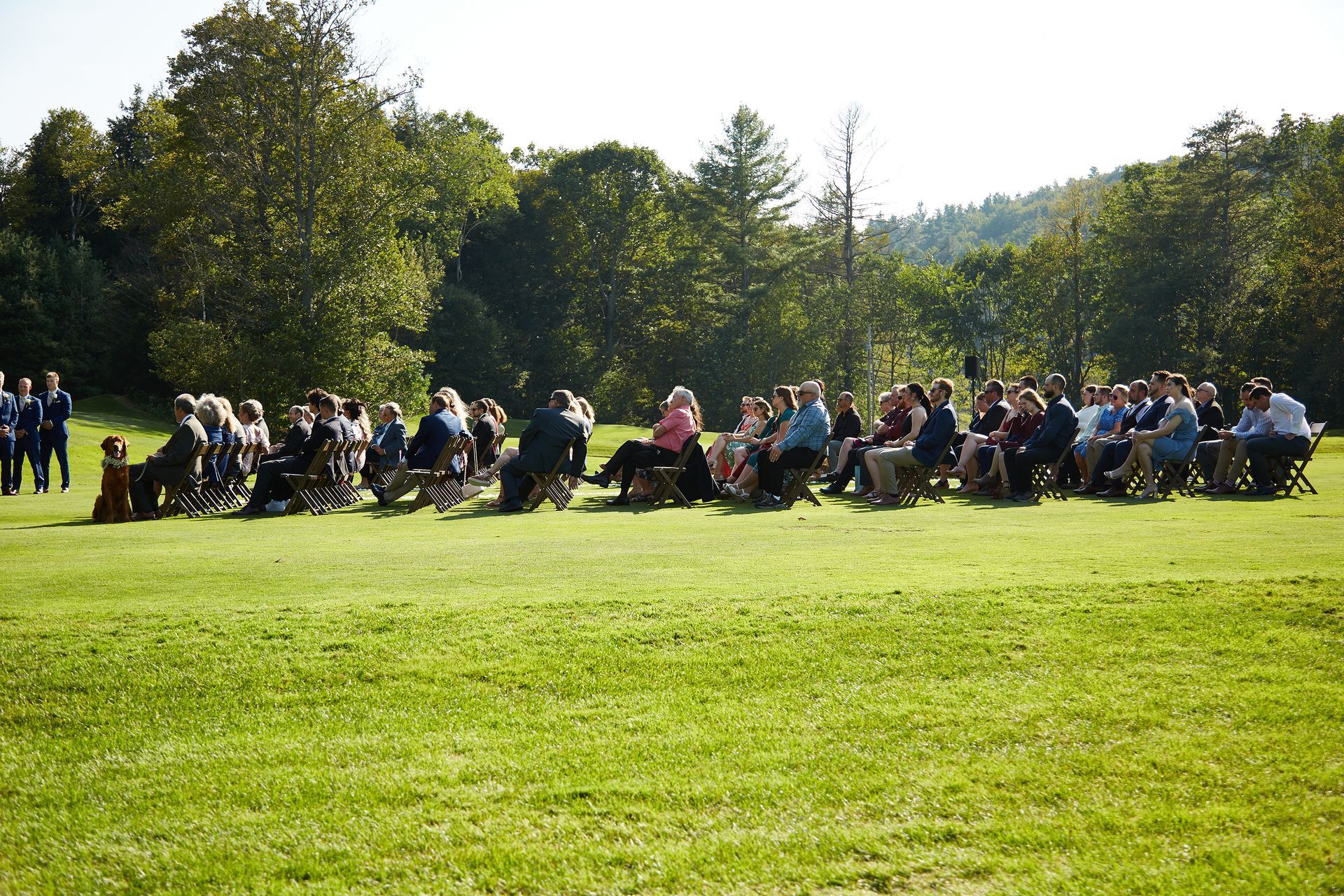 A large group of people are sitting in chairs in a grassy field.