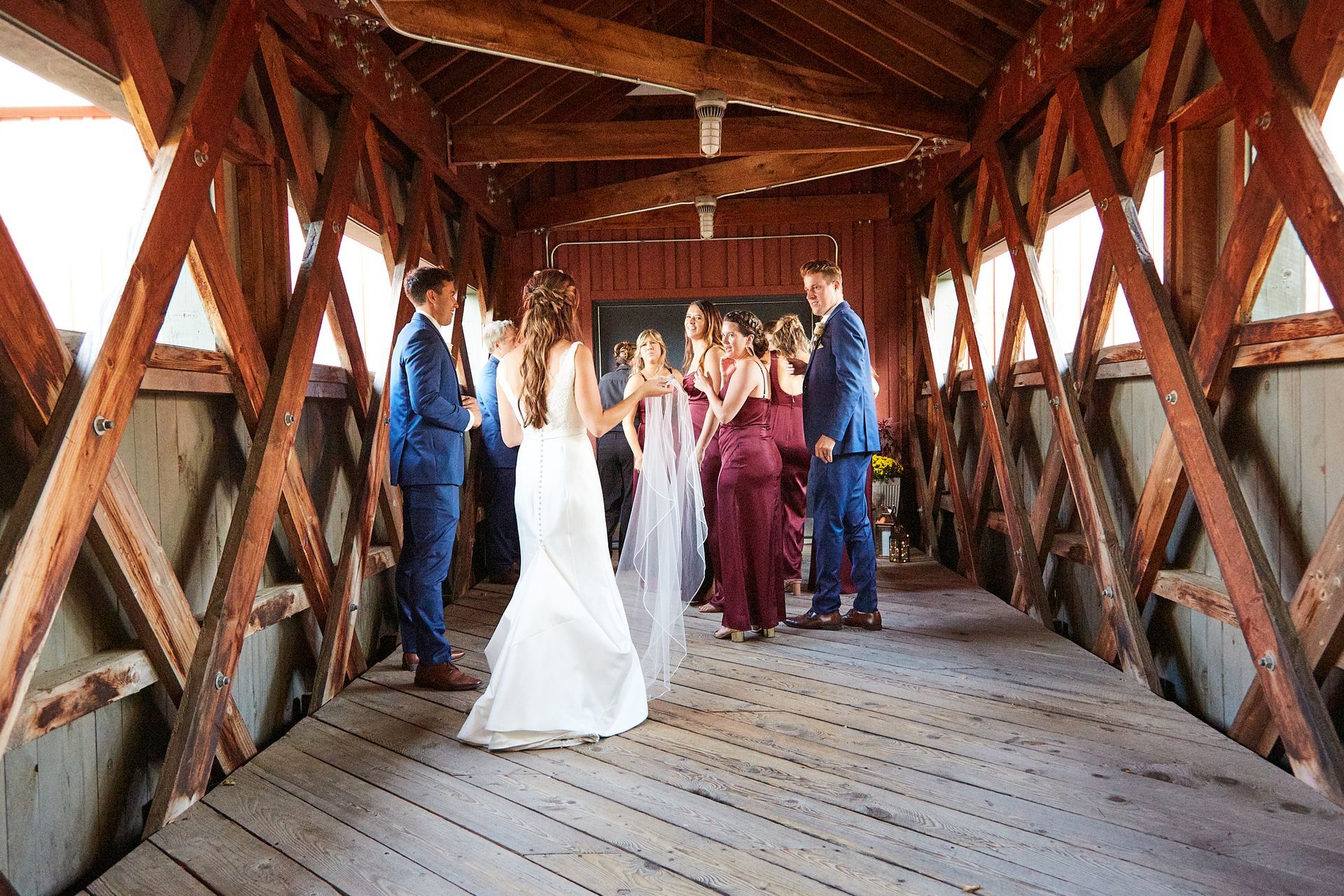 A bride and groom are dancing with their wedding party on a wooden bridge.