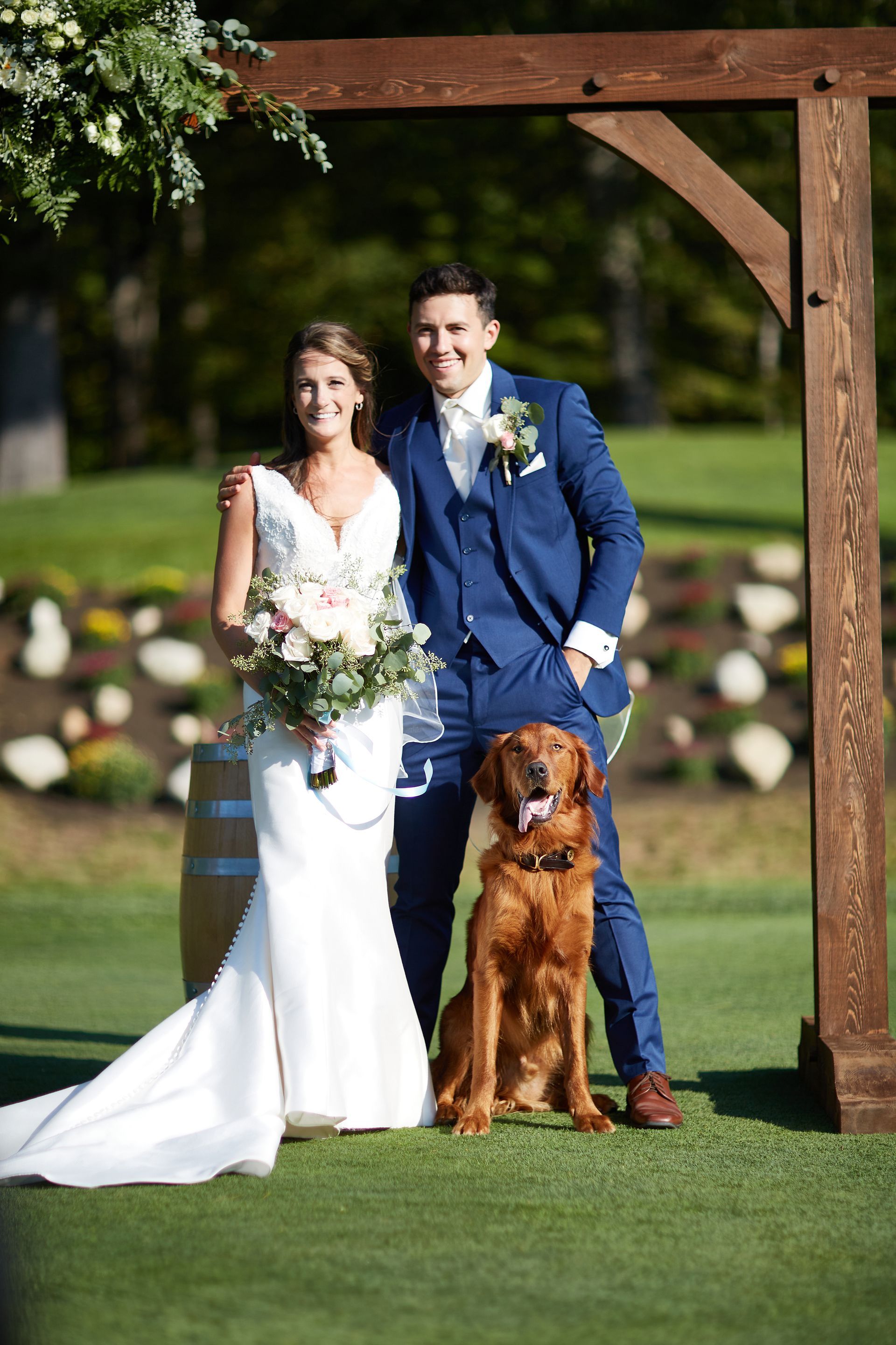 A bride and groom are posing for a picture with their dog.