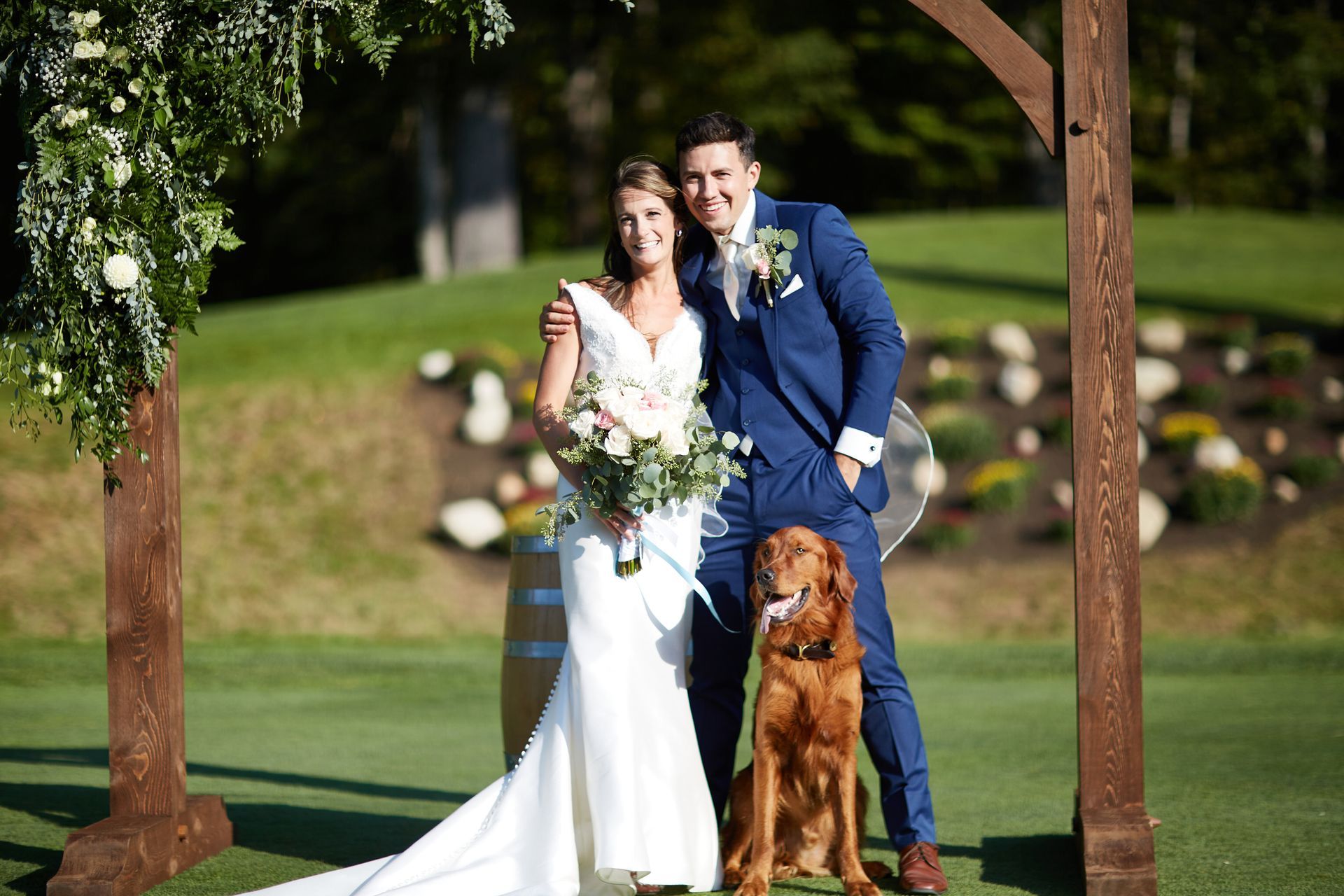 A bride and groom are posing for a picture with their dog.