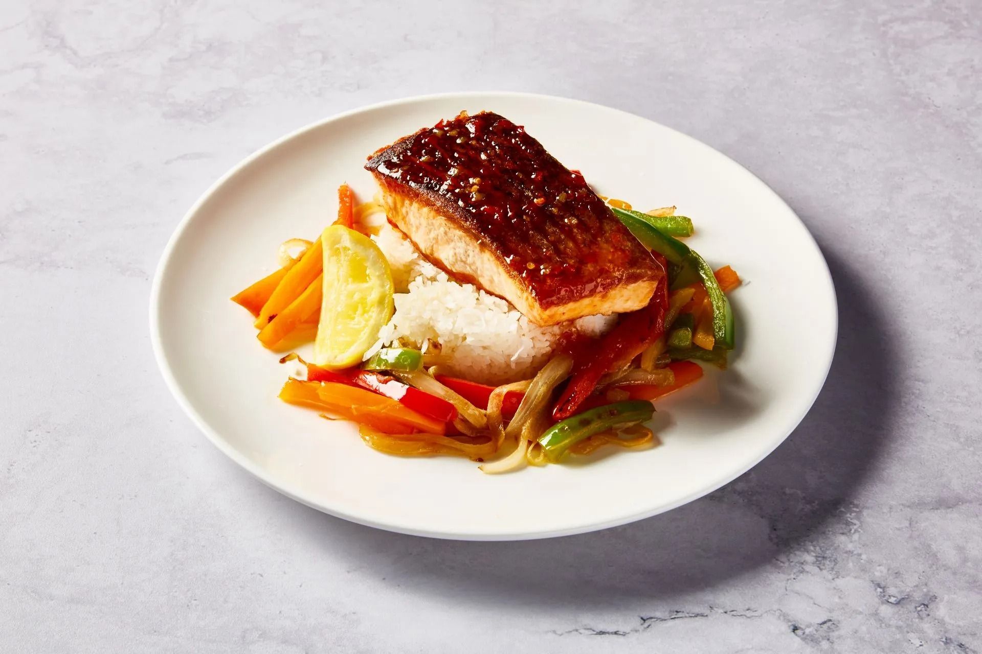 Salmon with glazed sauce, rice, and colorful stir-fry vegetables on a white plate.