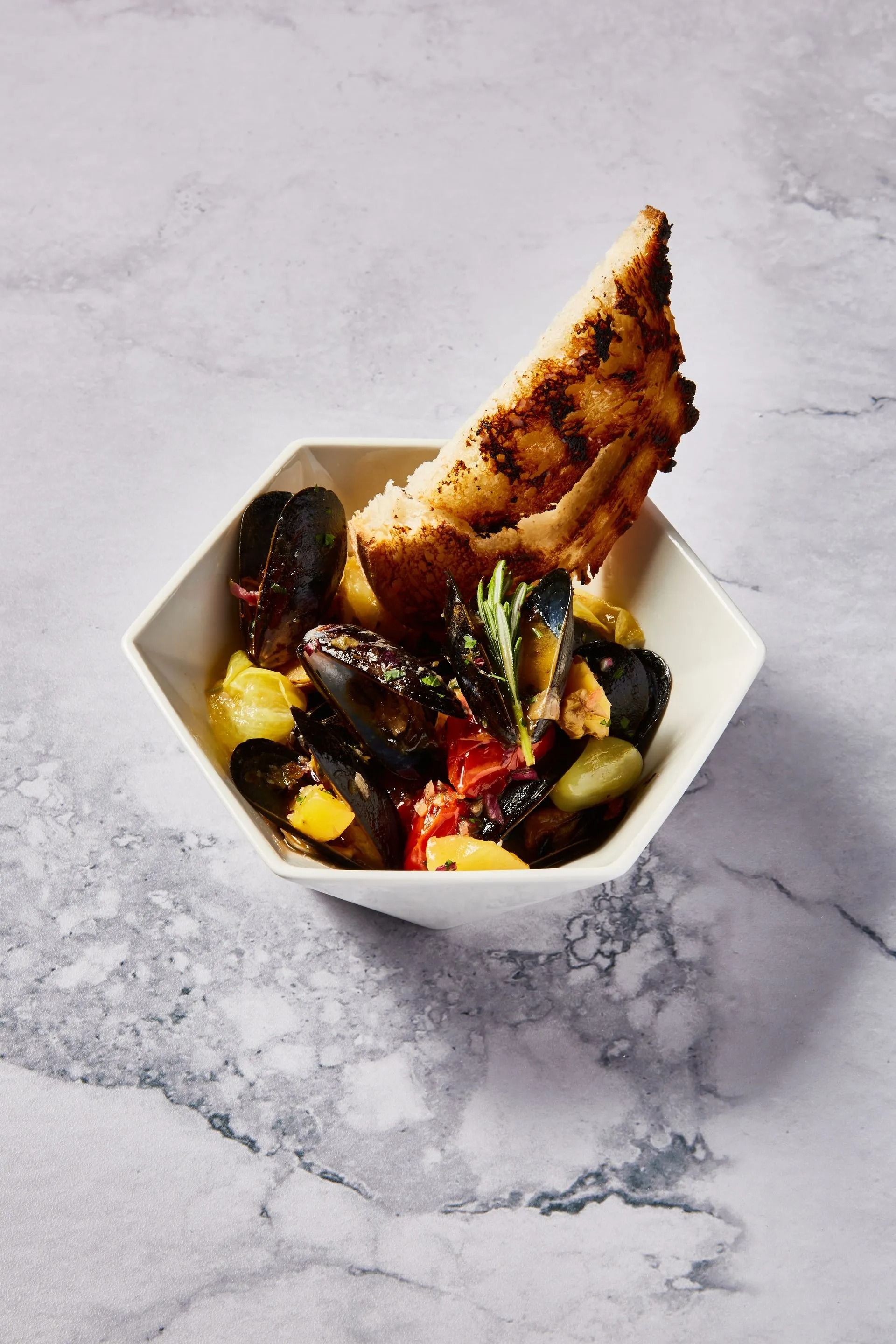 Bowl of mussels with vegetables and toasted bread.