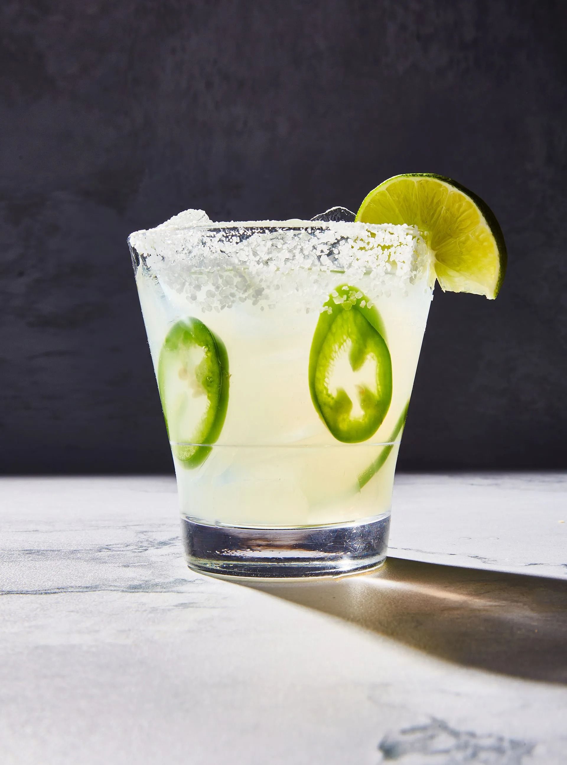 Spicy margarita in a glass rimmed with salt, garnished with lime and jalapeño slices.