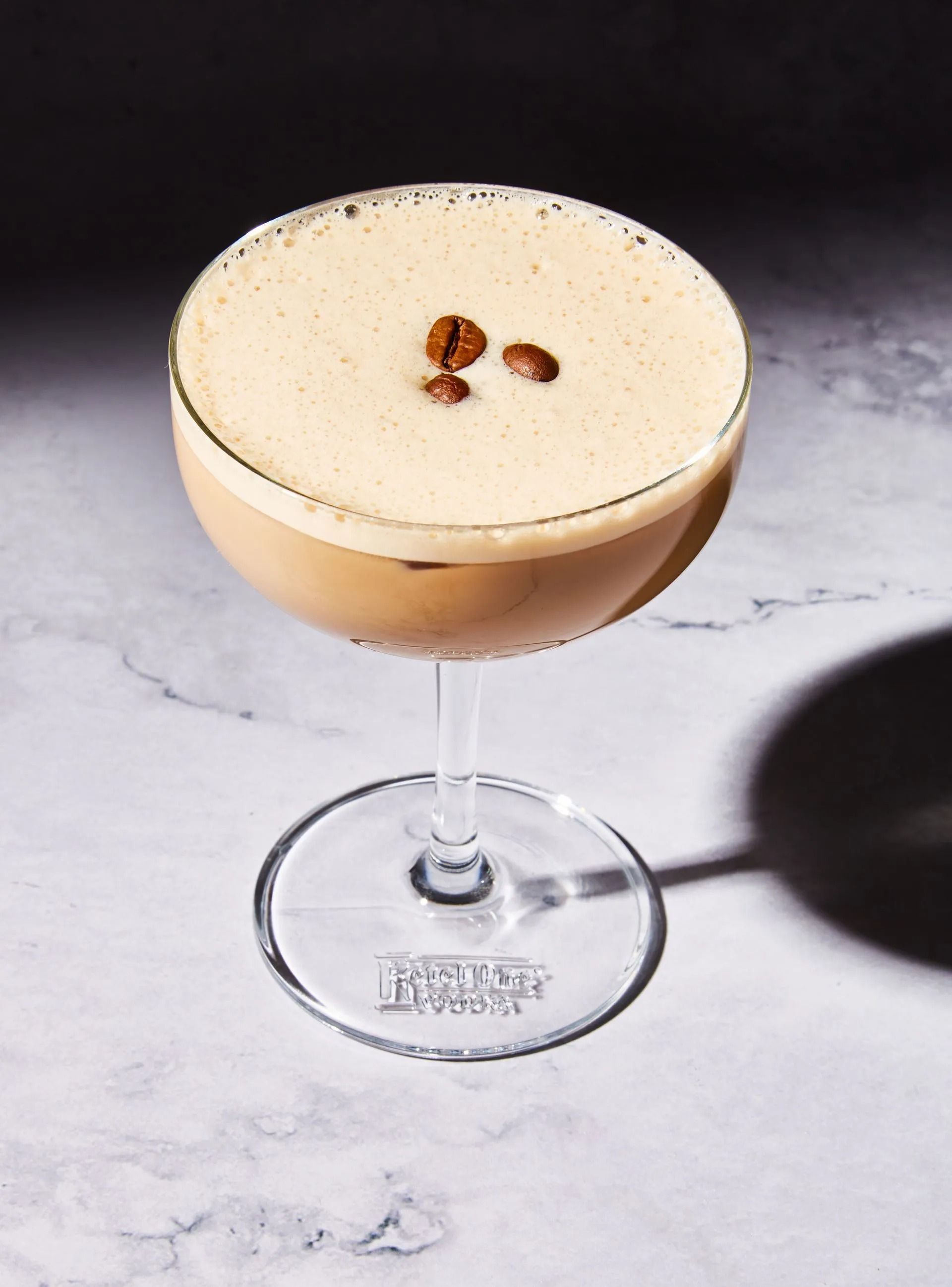 Espresso martini in a stemmed glass, topped with foam and coffee beans.
