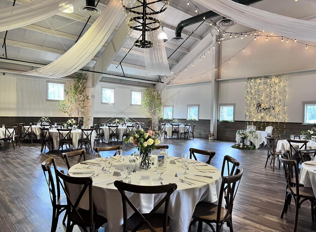Wedding reception venue: round tables set with white linens, wooden chairs, draped fabric, and decorative string lights.